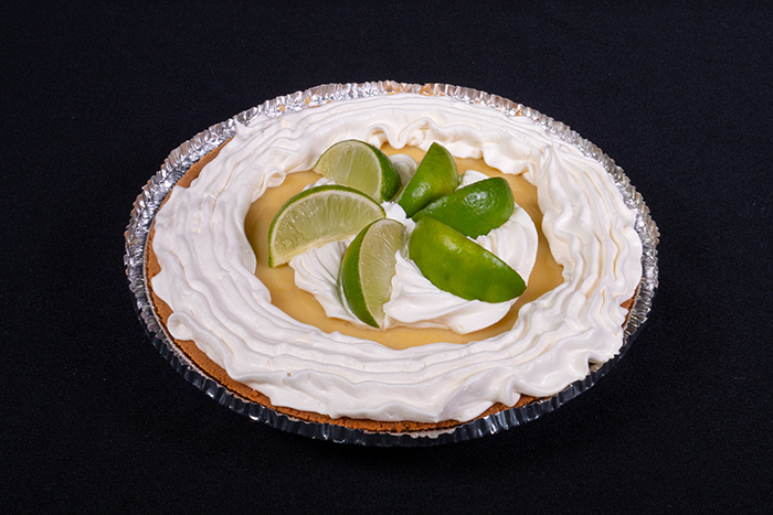 Delicious key lime pie with limes and whipped topping on top.